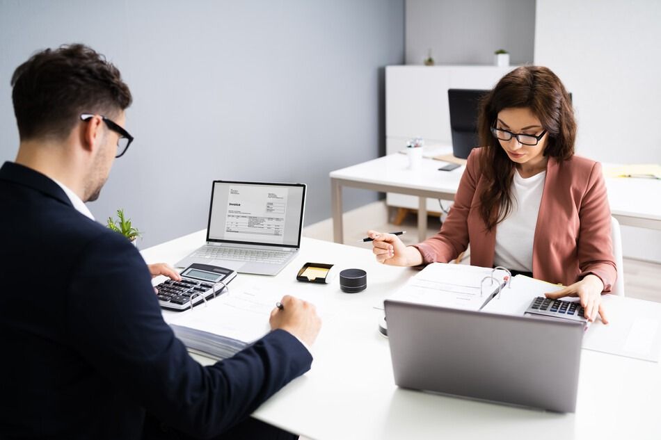 Un hombre y una mujer están sentados en un escritorio con computadoras portátiles.