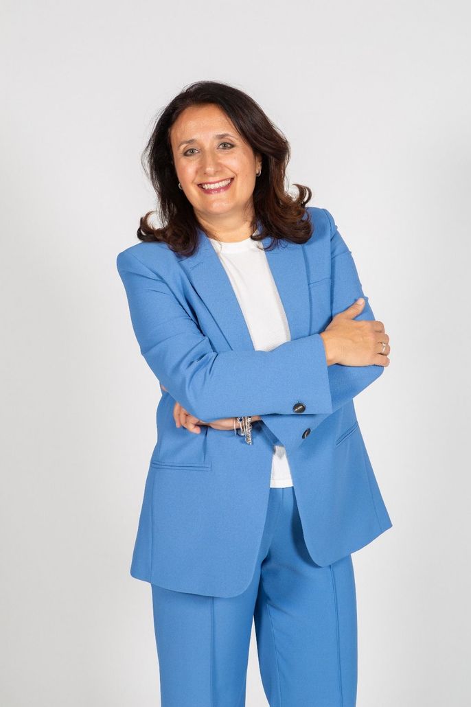 Una mujer con un traje azul está de pie con los brazos cruzados y sonriendo.