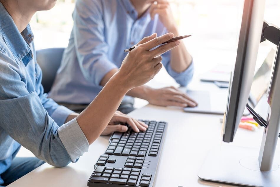 Dos personas están sentadas en un escritorio trabajando en una computadora.