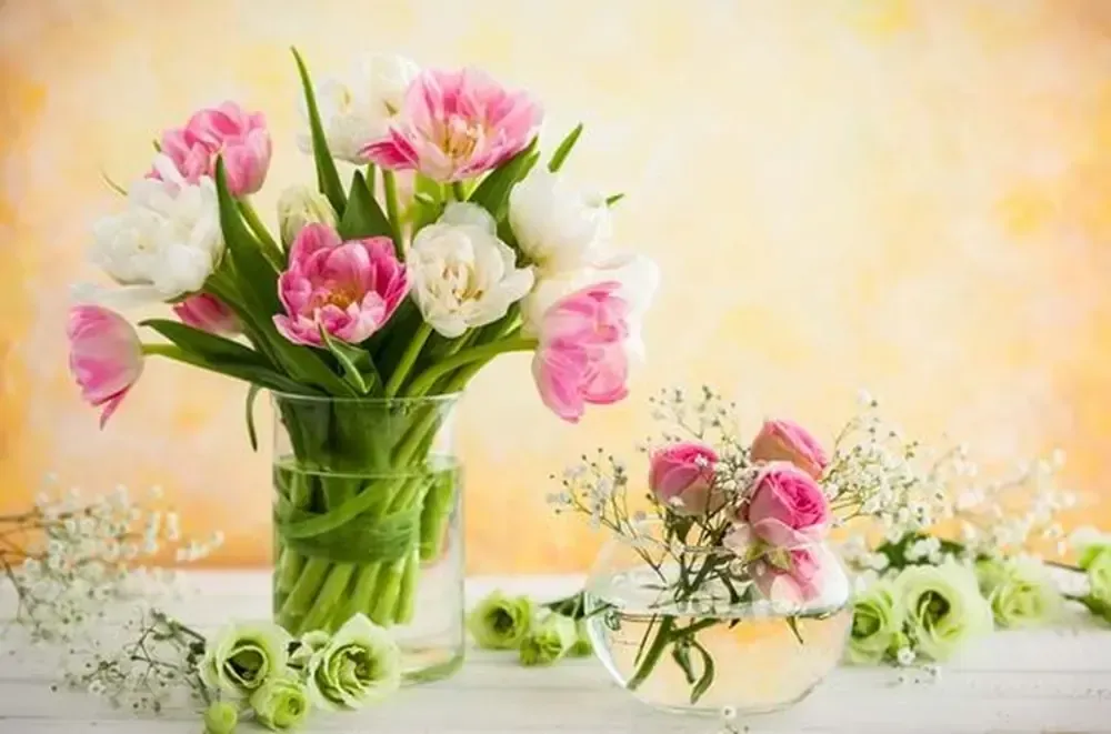 Ramo de tulipanes rosas y blancos en jarrón transparente; pequeño jarrón de cristal con rosas rosas; fondo amarillo.