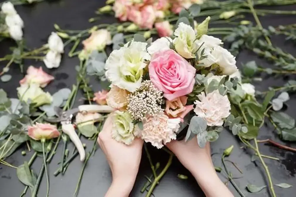 Manos sosteniendo un ramo con rosas rosadas y blancas, follaje verde.