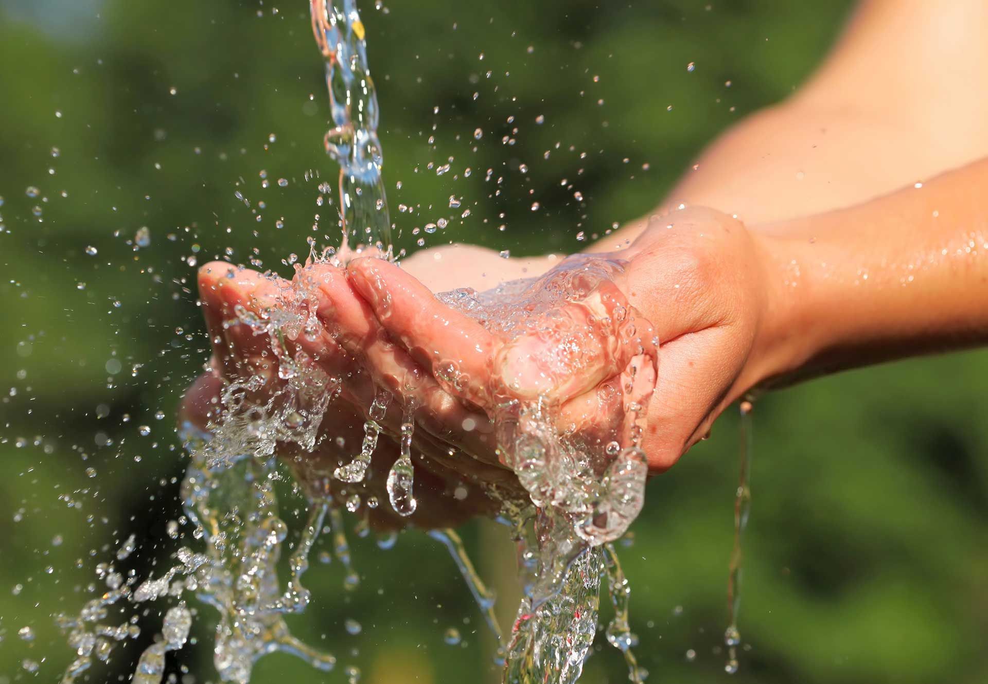 Des mains qui entourent l'eau qui coule, créant des éclaboussures, sur un fond vert flou.