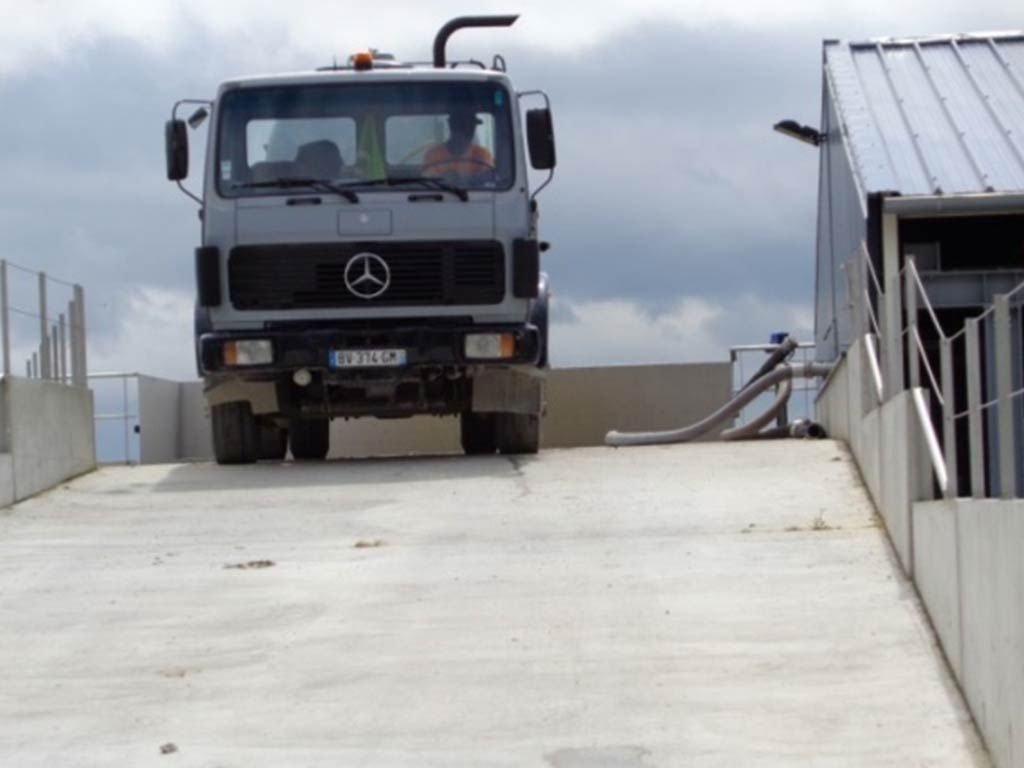 Un camion gris, une Mercedes, monte une rampe en béton. Le bâtiment se trouve à droite.