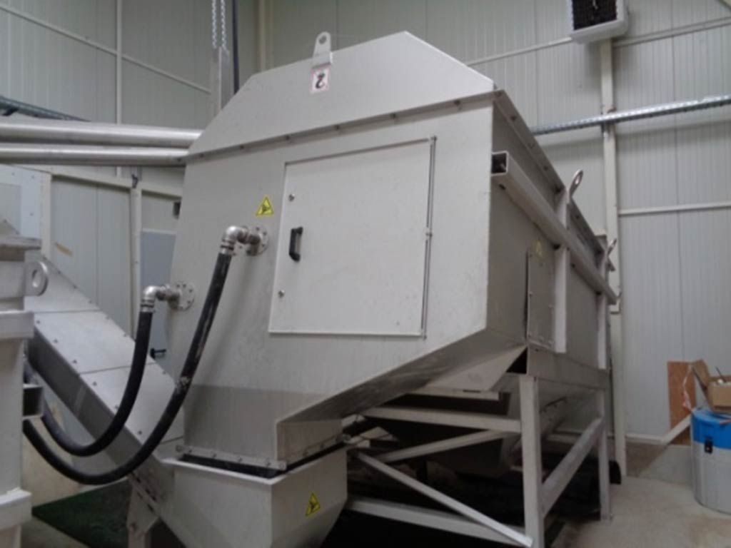 Grande machine industrielle en acier inoxydable dans un environnement d'usine, avec des tuyaux et une porte.