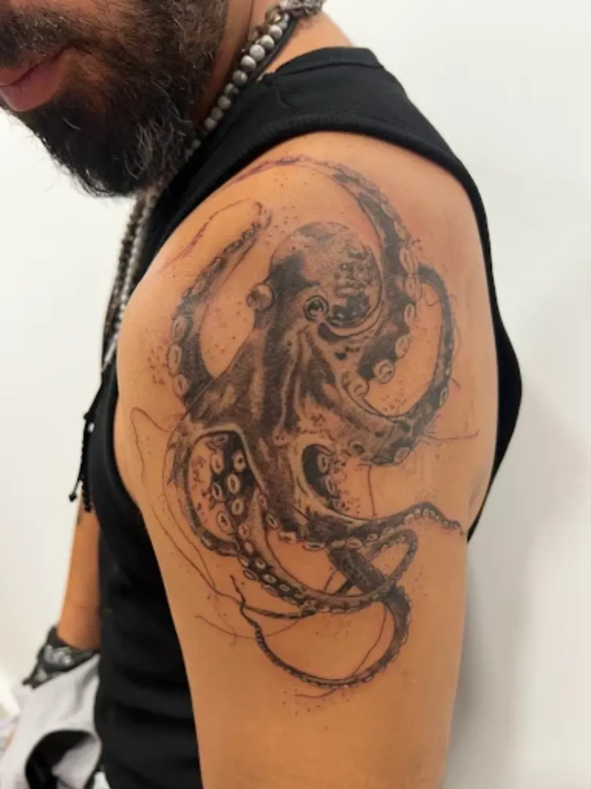Tatuaje de un pulpo negro en el hombro de una persona, con detalles abstractos de tinta, visto de cerca.
