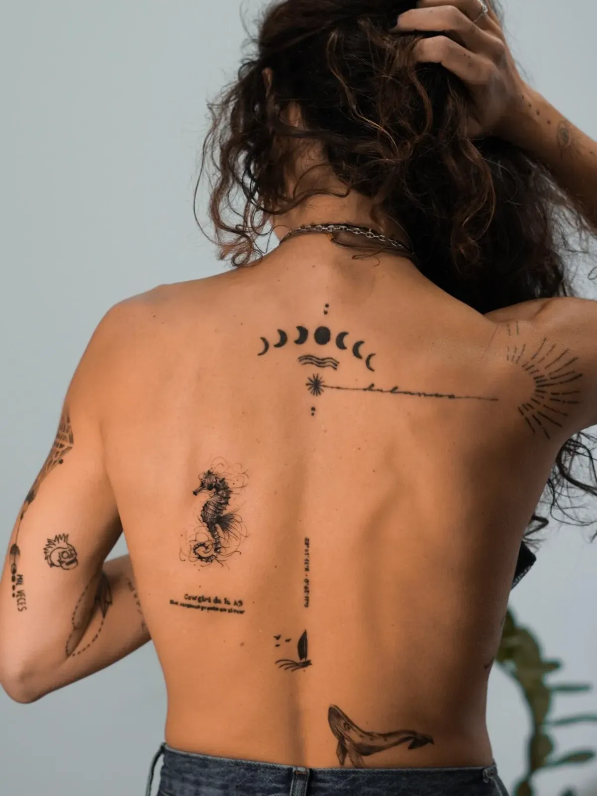 Persona con tatuajes en la espalda, incluidos un caballito de mar, una ballena y fases lunares.