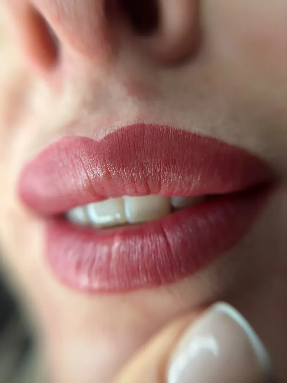 Persona con un tatuaje perforando la oreja de otra, ambas vestidas de negro. En un interior, cerca de una ventana.