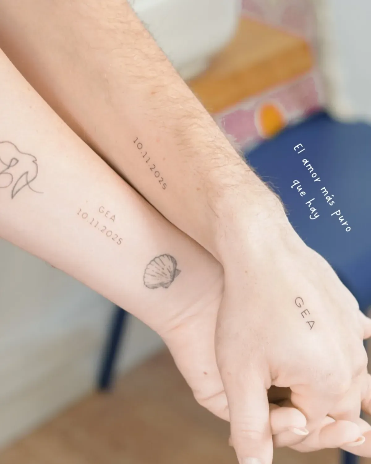 Dos brazos con tatuajes a juego, tomados de la mano. Se ven fechas y símbolos en las muñecas.