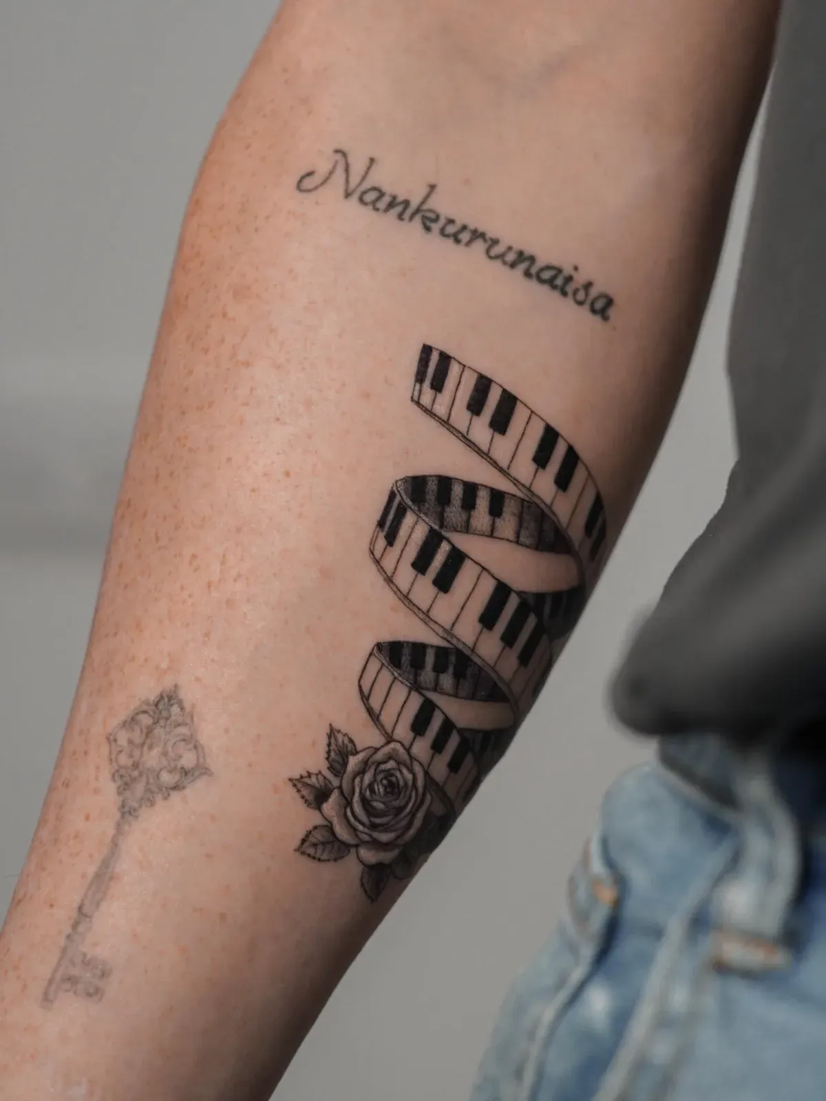 Tatuaje en el brazo: teclas de piano en espiral, una rosa y una inscripción que dice 