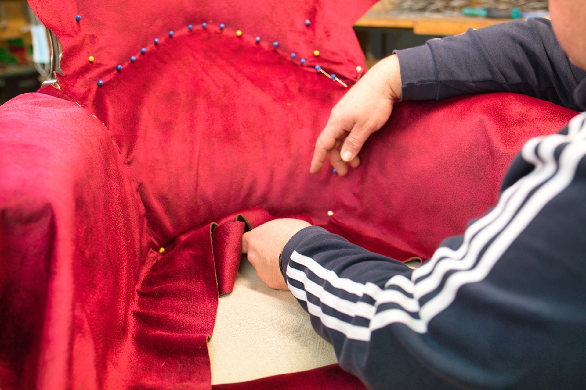 Un tapissier pendant la réfection d'un fauteuil au tissu rouge.