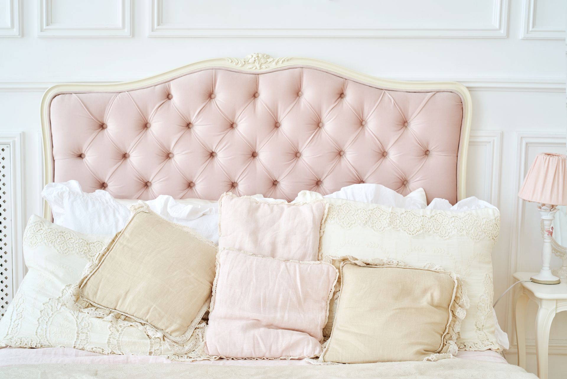 Lit avec tête de lit au tissu rose pâle.