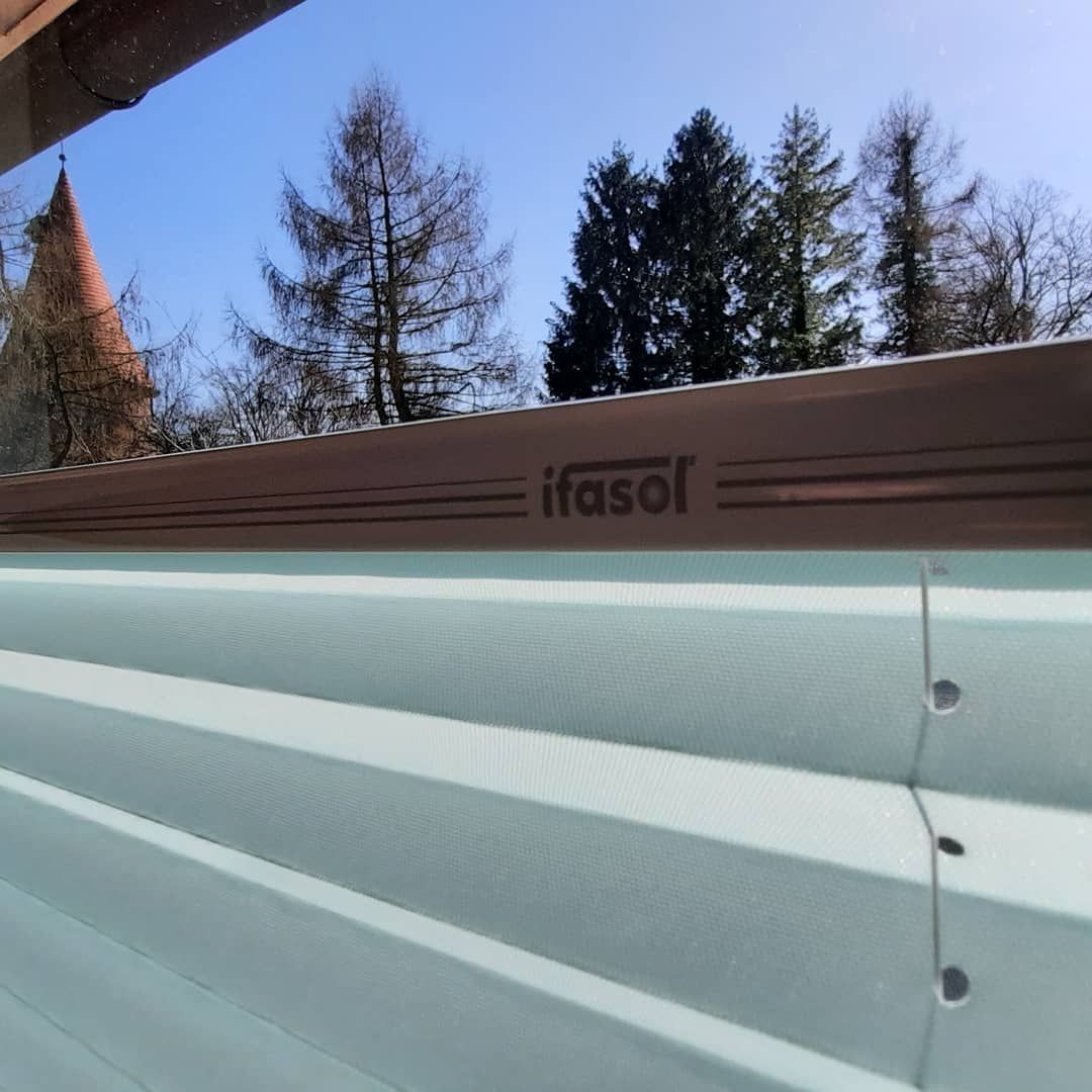 Eine Nahaufnahme einer Ifasol Jalousie mit Bäumen im Hintergrund