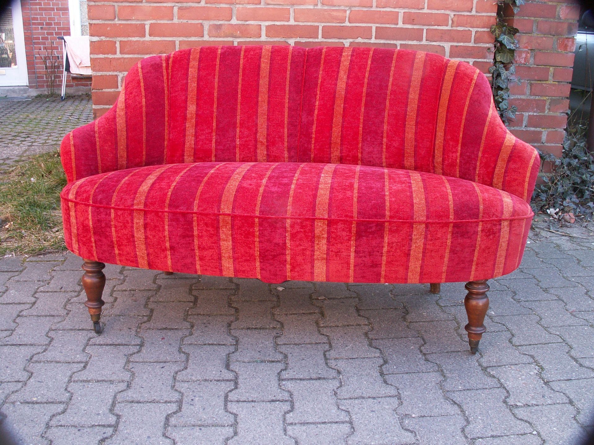 Eine rot gestreifte Couch steht auf einem Bürgersteig vor einer Backsteinmauer