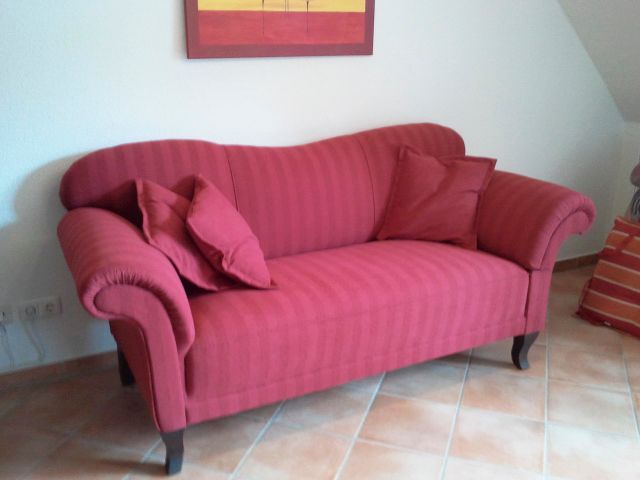 Eine rote Couch in einem Wohnzimmer mit einem Bild an der Wand darüber