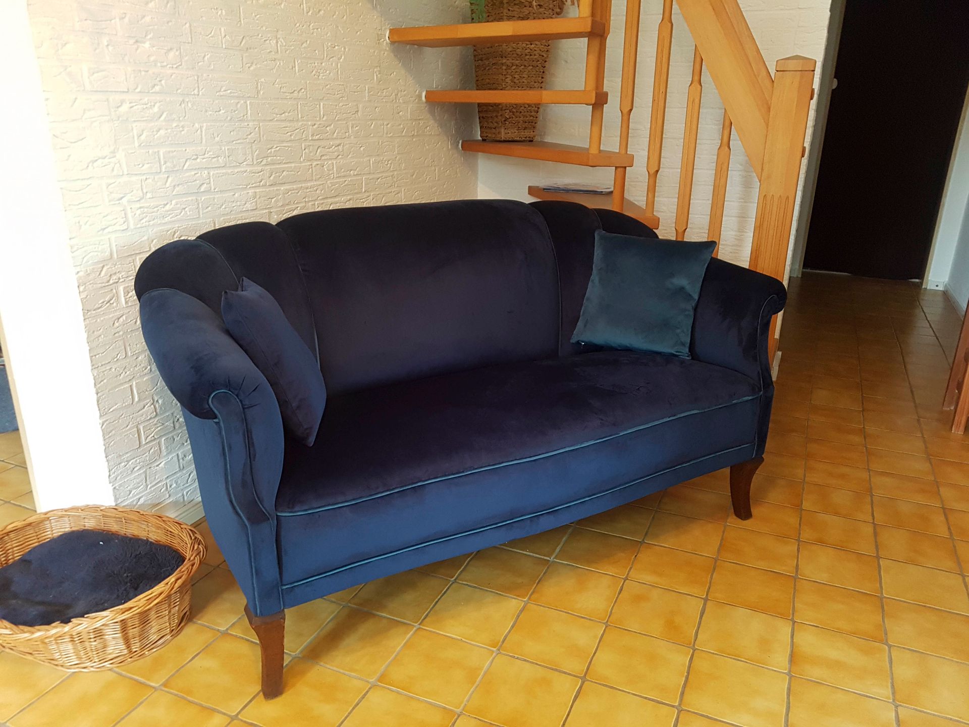 In einem Wohnzimmer steht neben einer Holztreppe ein blaues Sofa.