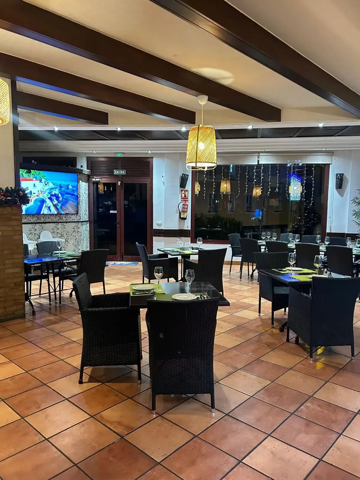 Vista interior de un restaurante vacío con sillas de mimbre negras, mesas cuadradas, suelos de baldosas 