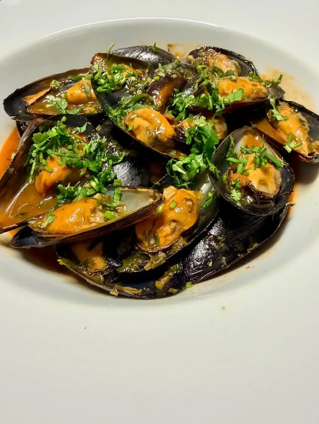 Un tazón de mejillones cocidos en un sabroso caldo con hierbas, servido en un plato blanco.