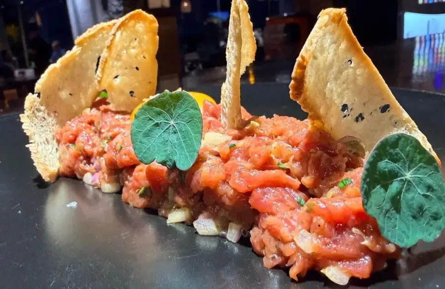 Panceta de cerdo crujiente sobre arroz sazonado, adornada con chips de vegetales morados, ramitas de hierbas