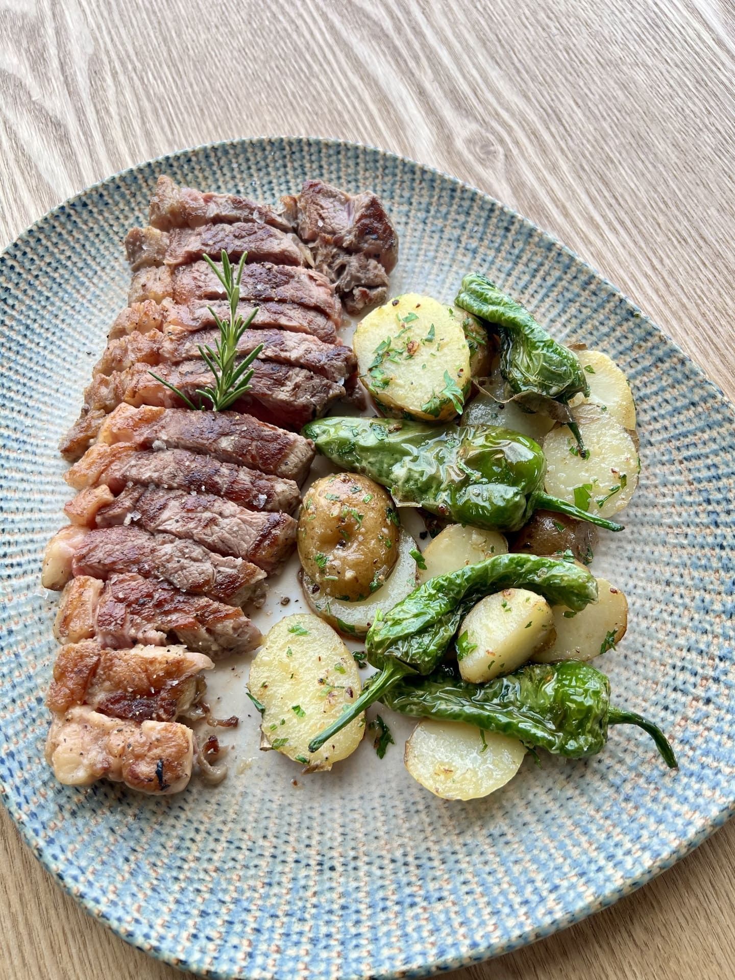 Filete a la parrilla en rodajas con patatas asadas y verduras verdes en un plato decorado.