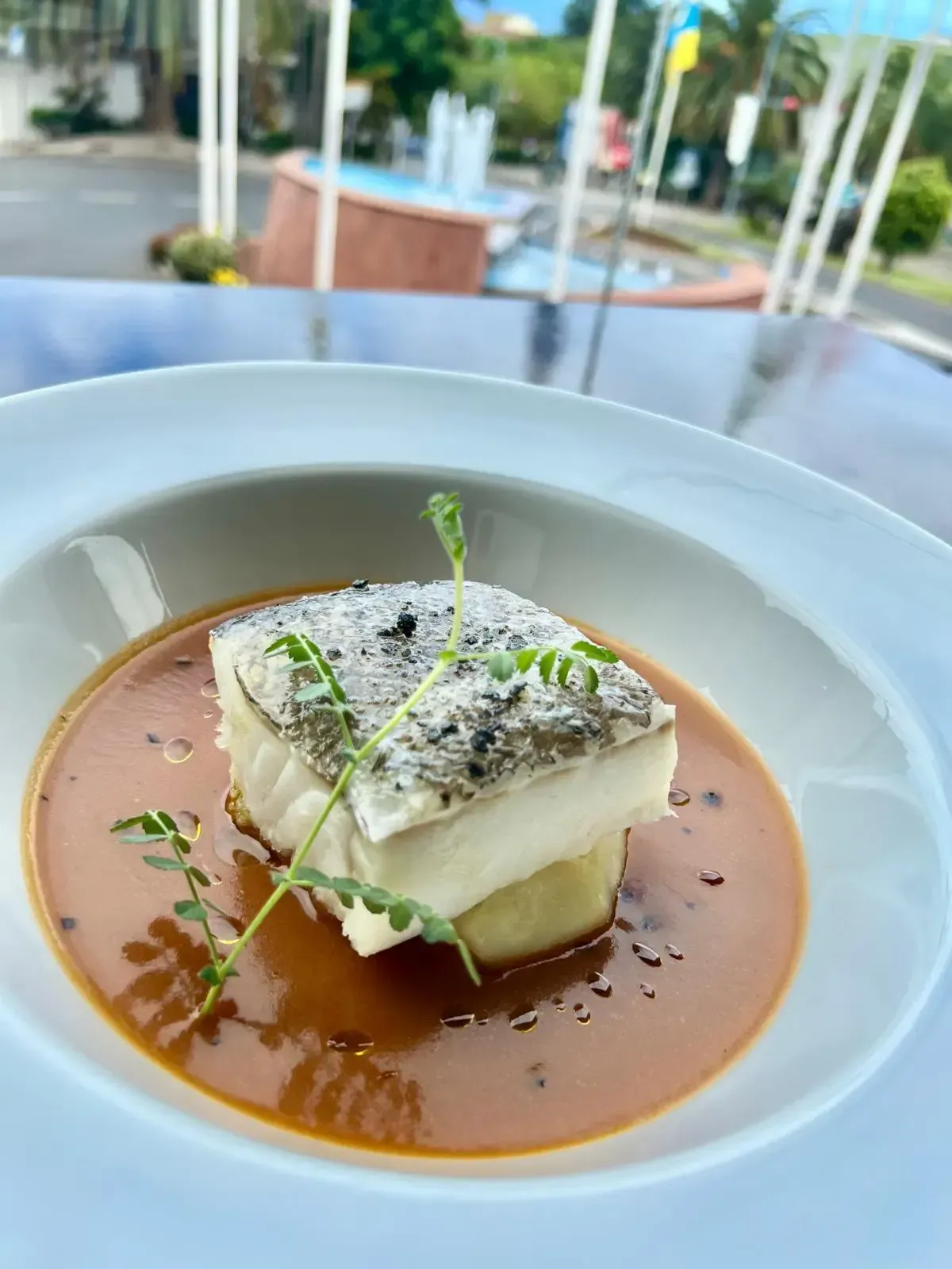 Un filete de pescado blanco a la plancha servido sobre una patata pequeña en una sabrosa salsa marrón