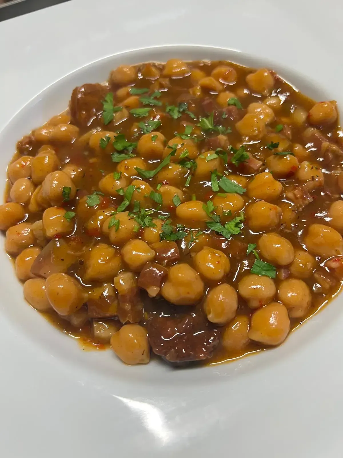 Un cuenco blanco lleno de un guiso caliente de garbanzos adornado con hierbas frescas picadas.