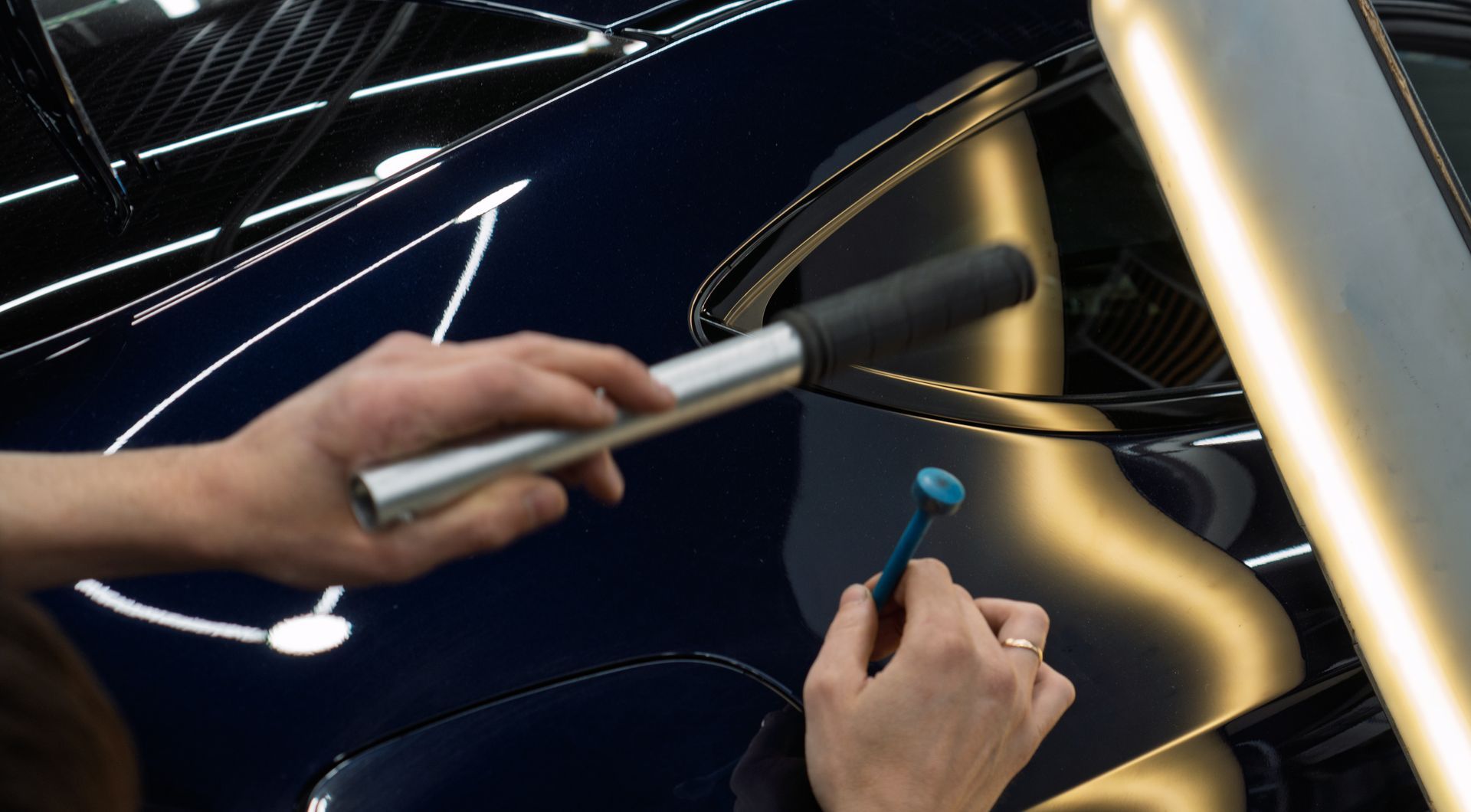 Une main utilisant un stylet sur une surface noire brillante, avec une lampe argentée allumée à proximité
