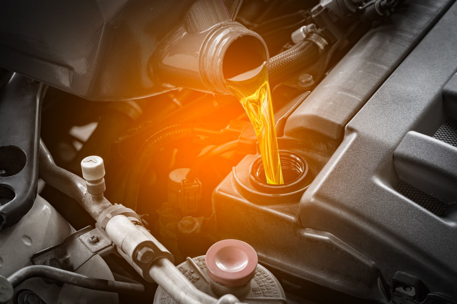 De l'huile moteur est versée dans un moteur de voiture ; le liquide est d'un orange incandescent et les composants du moteur sont visibles.