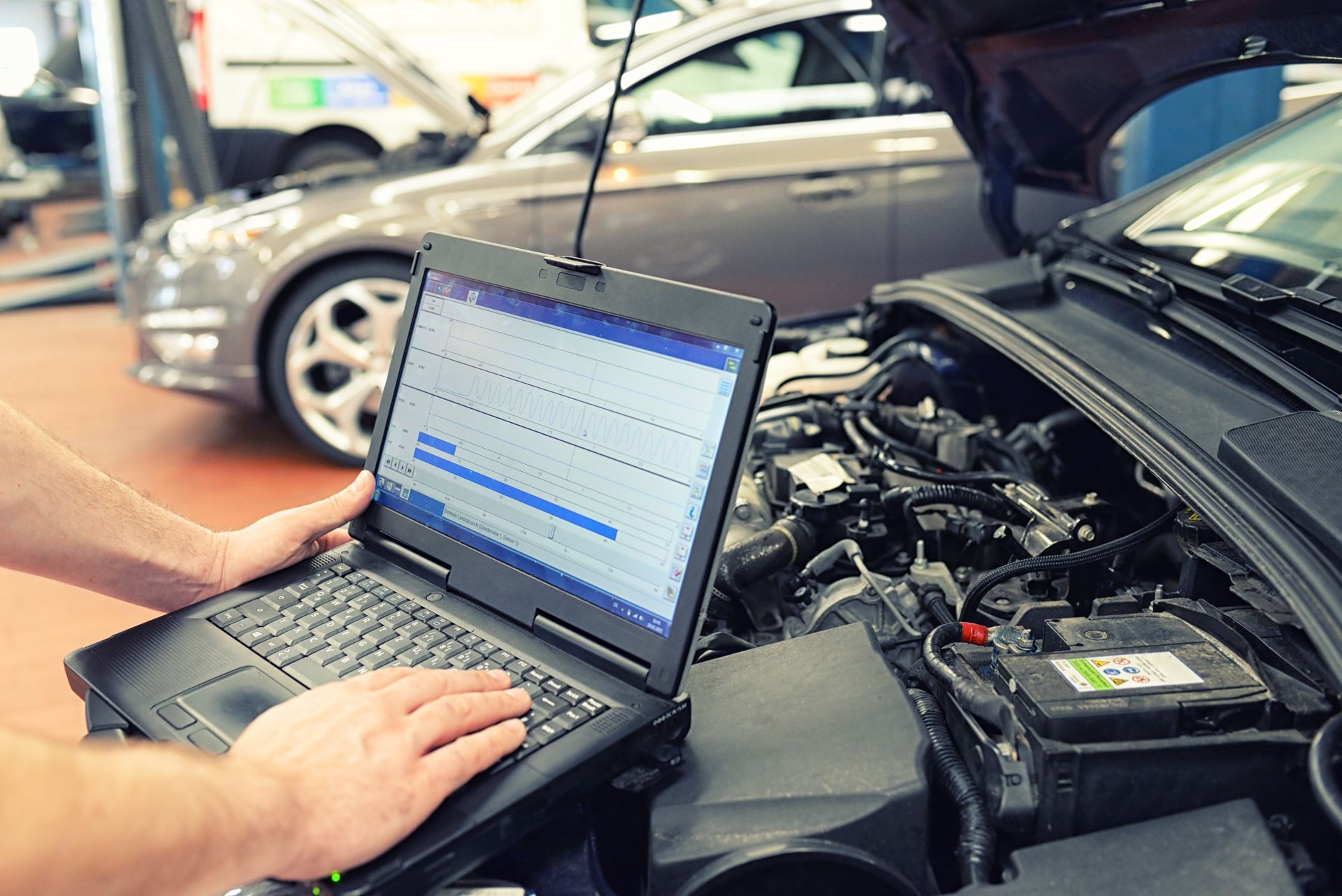 Un mécanicien utilise un ordinateur portable pour diagnostiquer un moteur de voiture dans un atelier de réparation automobile.