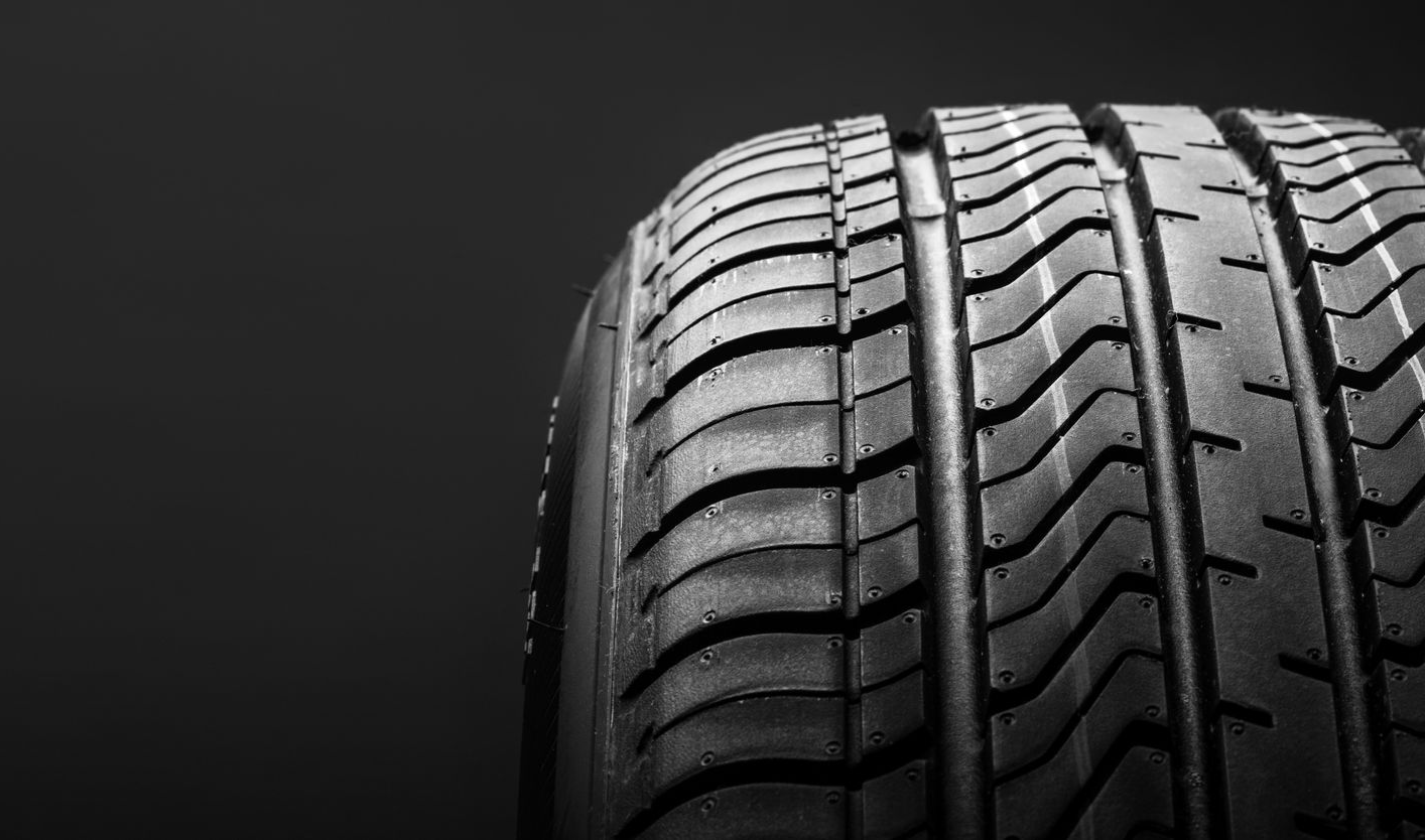 Gros plan sur la bande de roulement d’un pneu de voiture noir, sur fond sombre