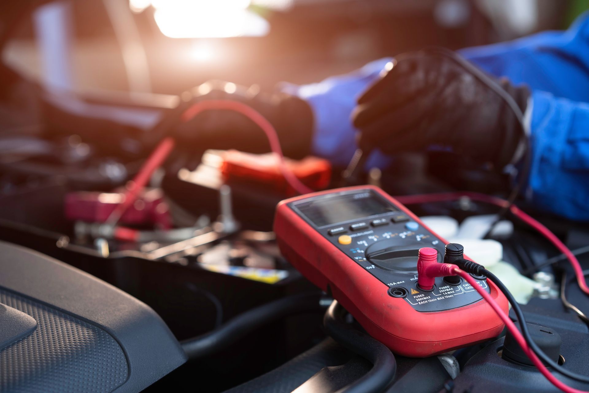 Installation pour le démarrage d’appoint d’une batterie de voiture, avec un multimètre rouge et des cordons de test dans le compartiment moteur