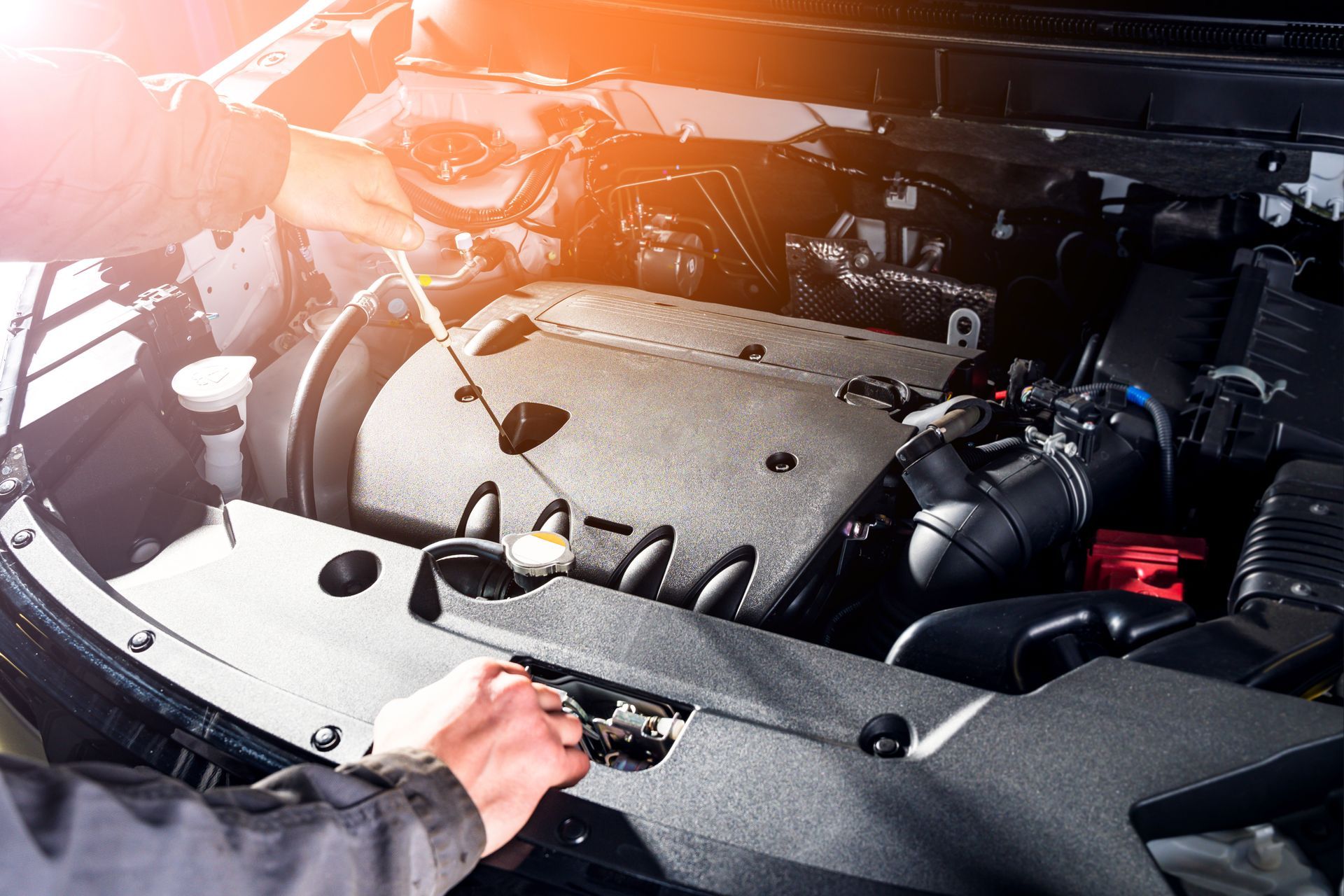 Inspection manuelle du compartiment moteur d'une voiture en plein soleil, avec les durites et les composants du moteur visibles.