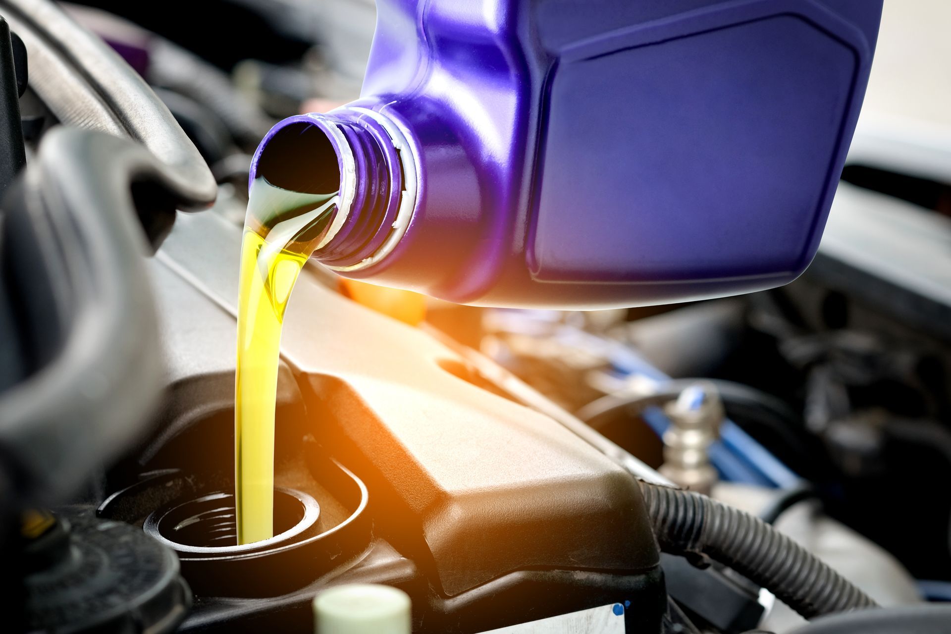 De l'huile moteur se déverse d'un bidon bleu dans un moteur, avec une lueur orange vif en dessous.