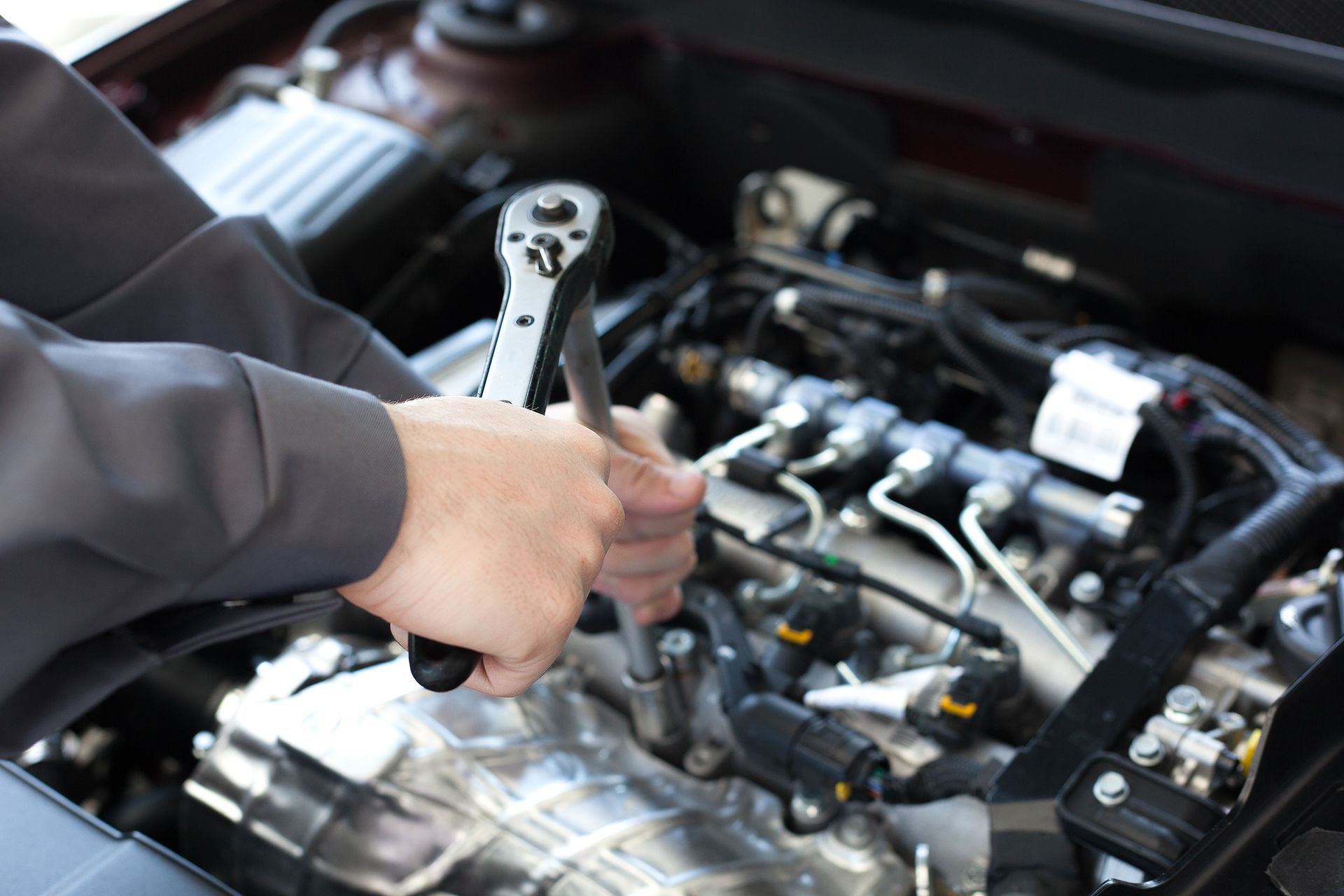 Un mécanicien qui resserre un boulon de moteur sous le capot ouvert d’une voiture à l’aide d’une clé à cliquet