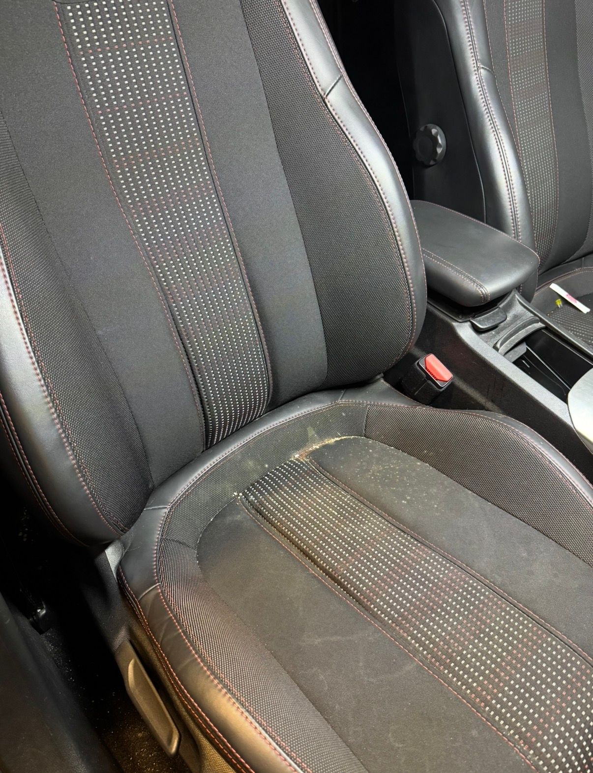 Gros plan sur le siège avant d'une voiture, avec un revêtement en tissu foncé et une usure visible sur le coussin.