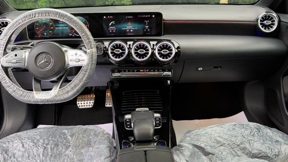 Intérieur moderne avec sièges noirs, volant Mercedes et aérateurs circulaires sur le tableau de bord propre.