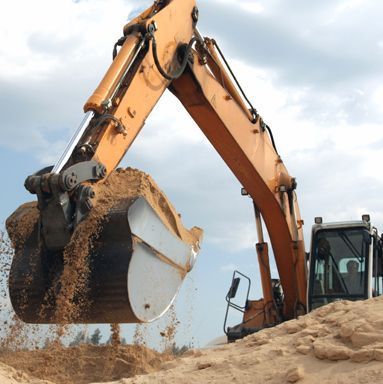 Una excavadora naranja levantando un gran cubo de metal lleno de arena contra un cielo nublado.