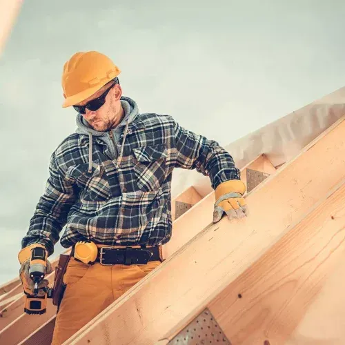Un homme utilise une perceuse sur un toit en bois.