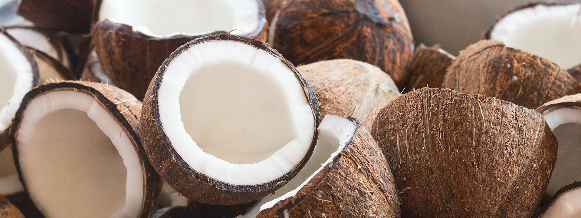Noix de coco coupées en deux ou entières avec une chair blanche et des coques brunes.