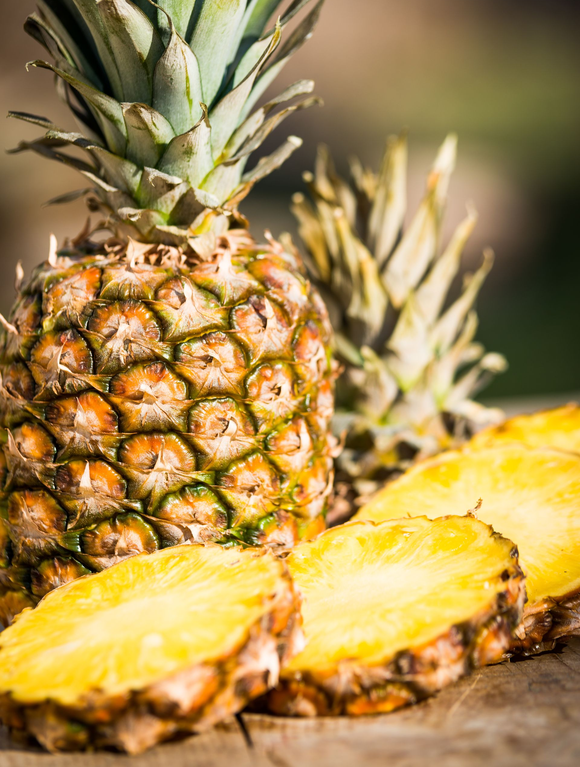 Un ananas entier et un ananas tranché posés sur du bois.