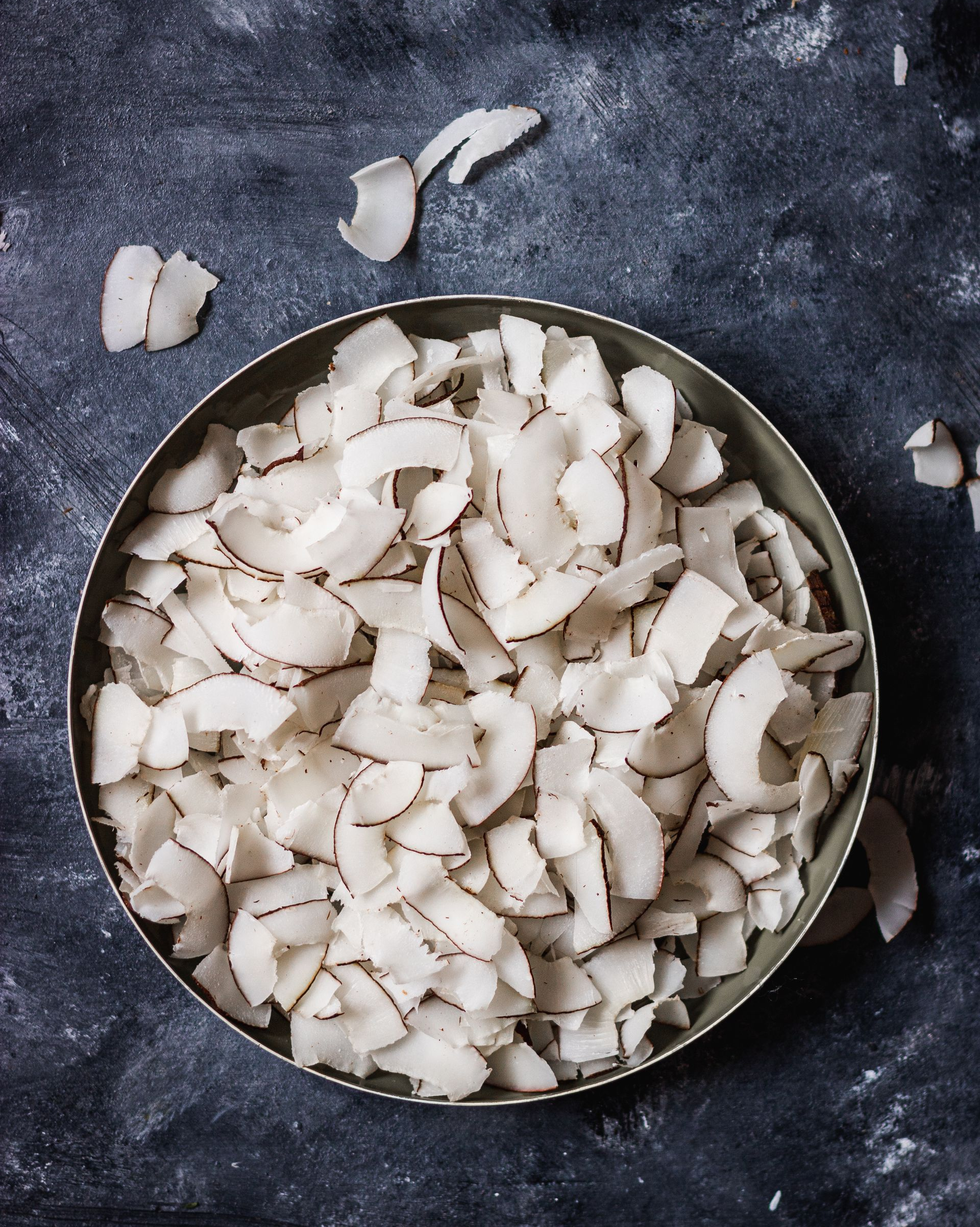 Bol de flocons de noix de coco grillés sur une surface texturée foncée.