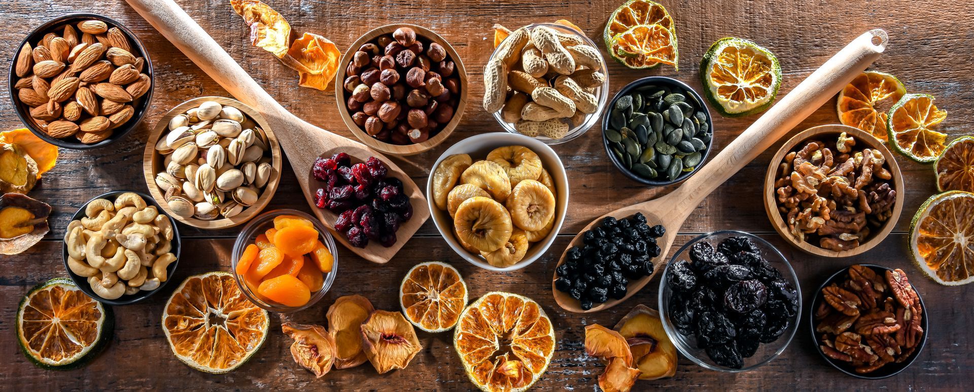 Divers fruits secs et noix disposés dans des bols sur une surface en bois.