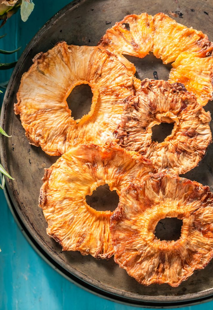 Rondelles d'ananas séchées dans un panier tressé, avec un ananas en arrière-plan.