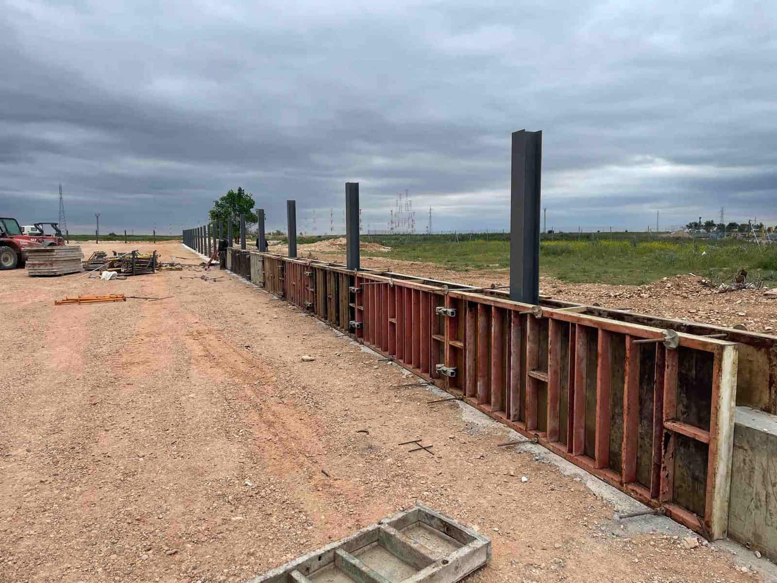 Obra: encofrados de hormigón para un muro, con tierra, soportes metálicos y cielo gris.