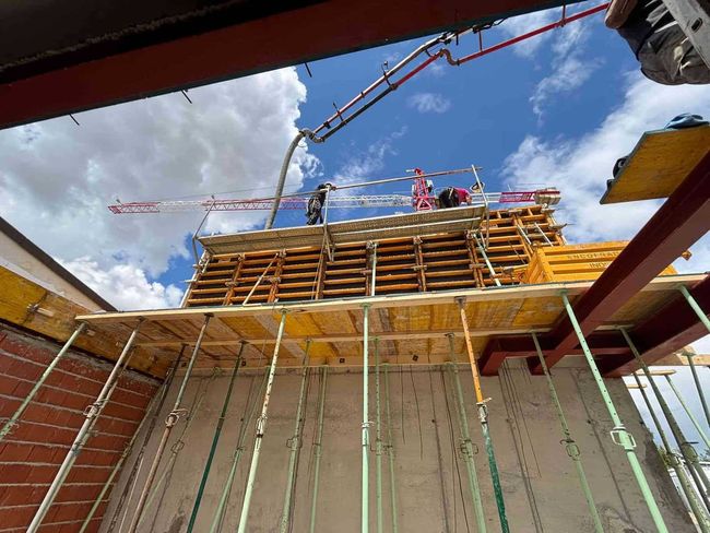 Obreros de la construcción vierten hormigón desde una bomba de pluma sobre una estructura de encofrado de madera. 