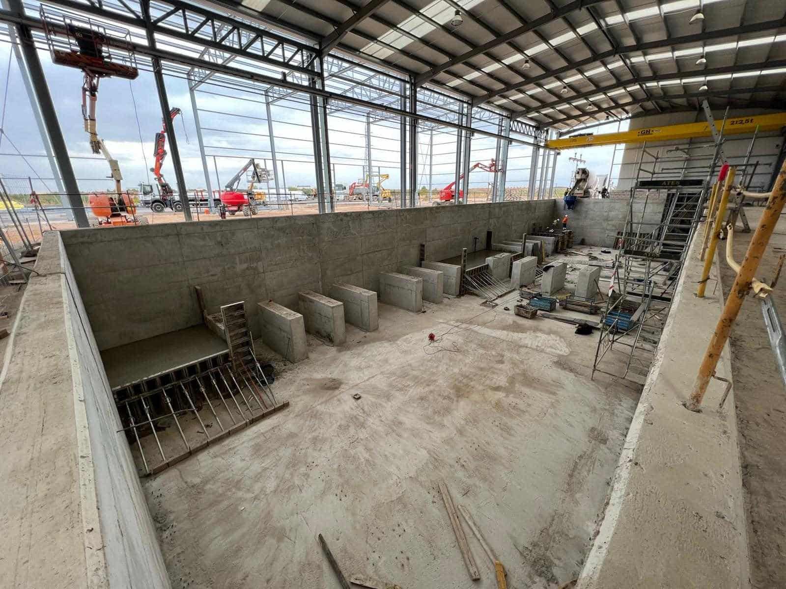 Obra de construcción con muros y encofrados de hormigón en el interior de una gran nave industrial.