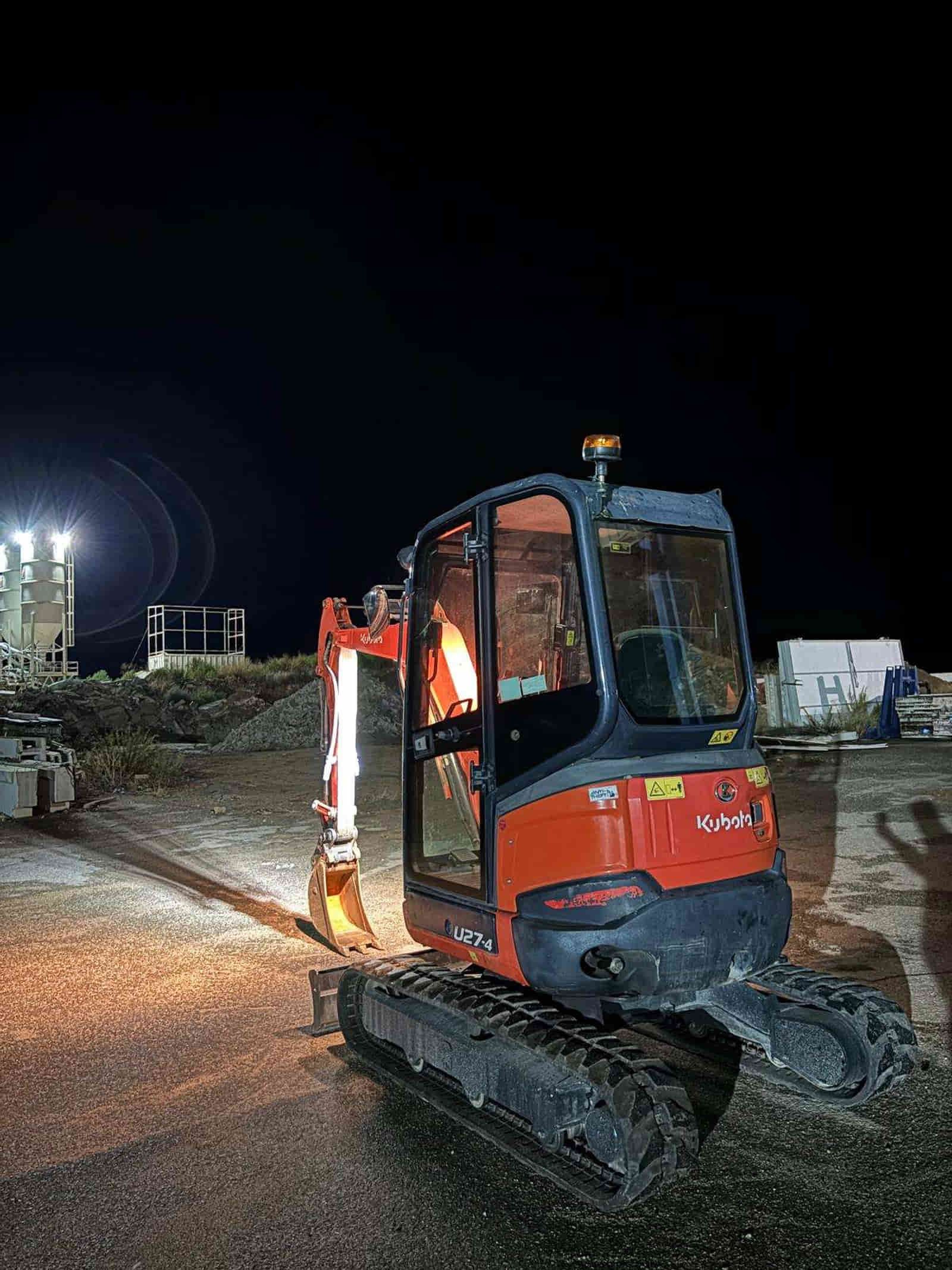 Excavadora Kubota naranja de noche con luces encendidas.