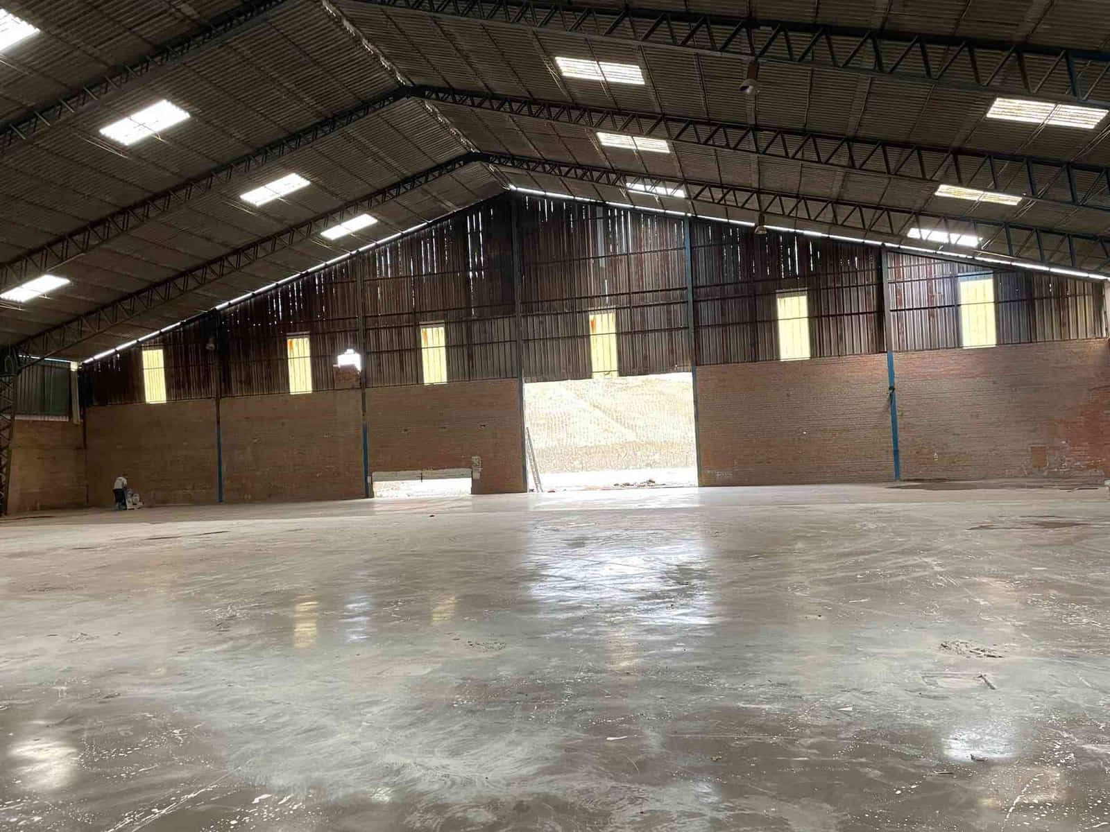 Dentro de un gran almacén vacío con piso de concreto, paredes de ladrillo y techo de metal corrugado.