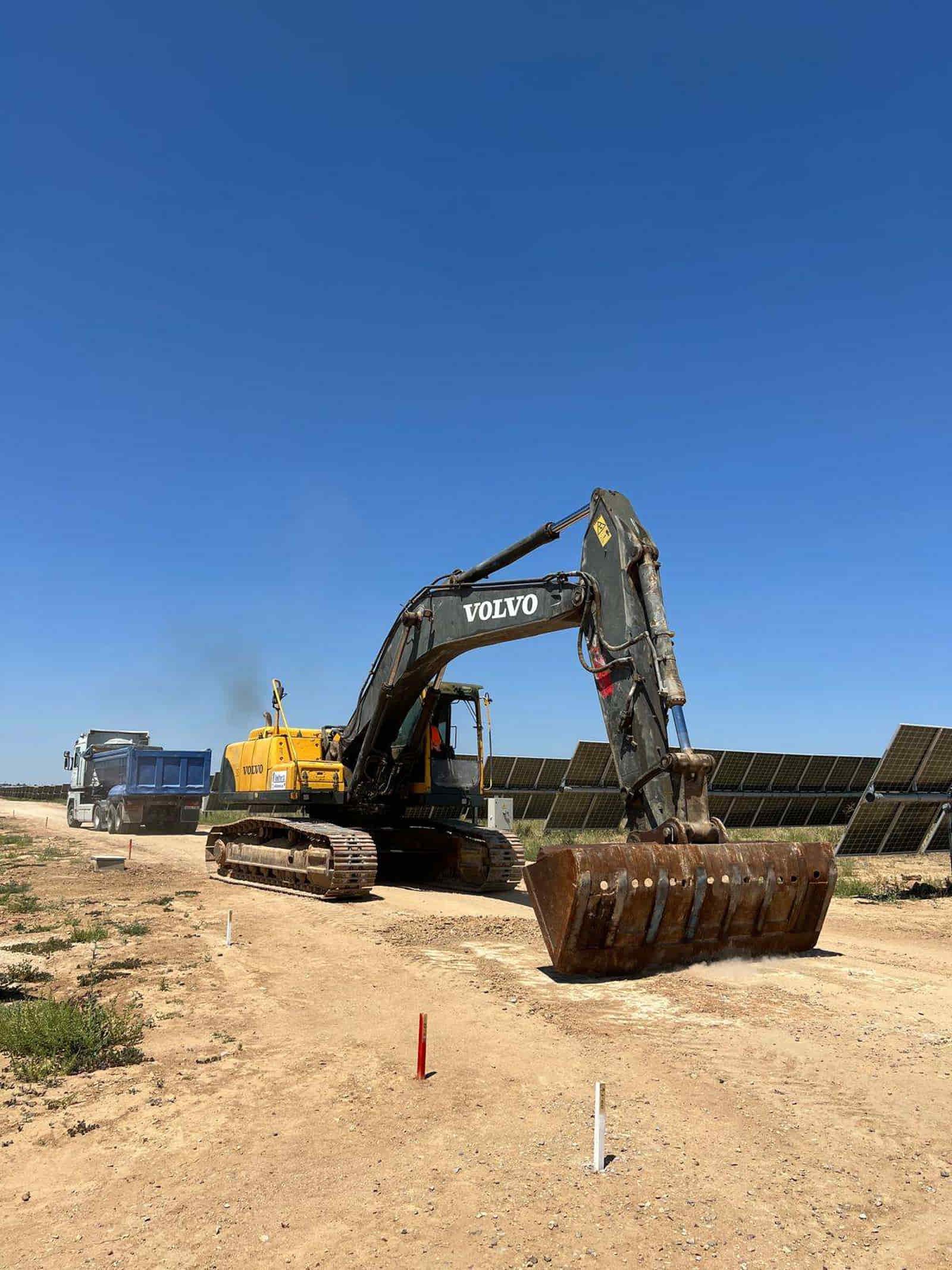 Excavadora en un camino de tierra, trabajando en una granja solar en un día soleado.