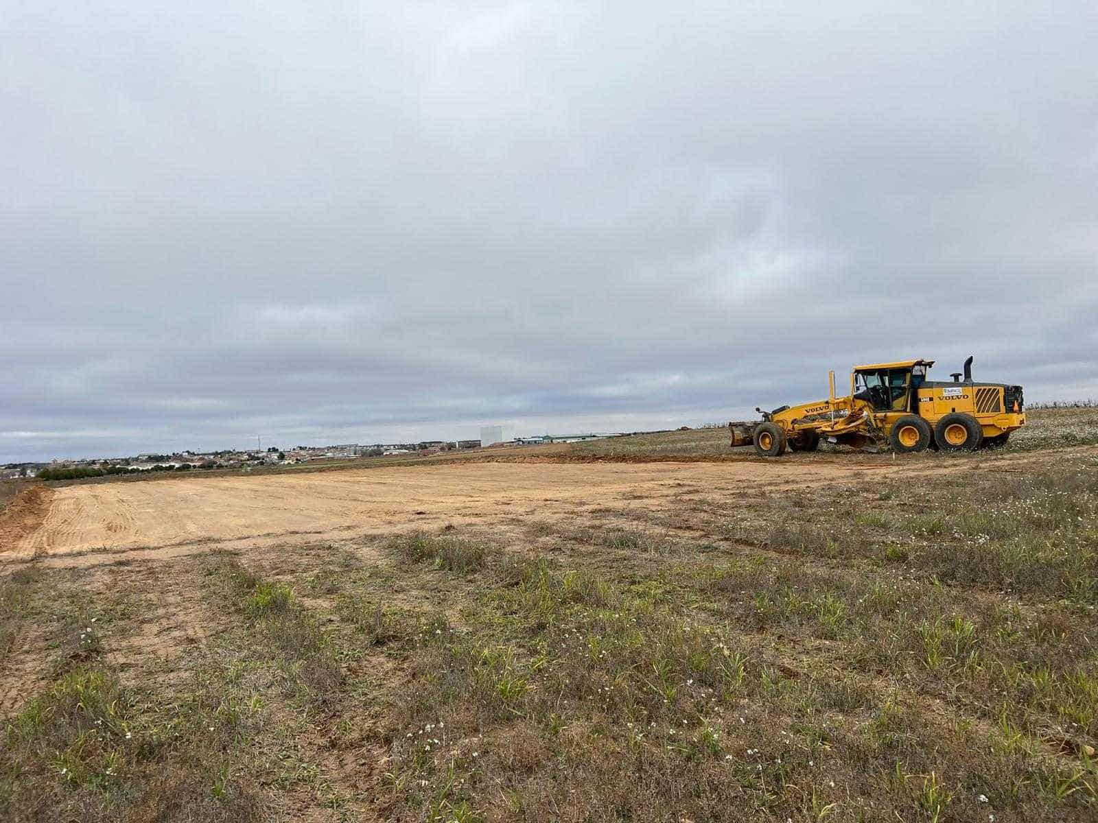 Motoniveladora amarilla alisando la tierra en un campo en un día nublado.