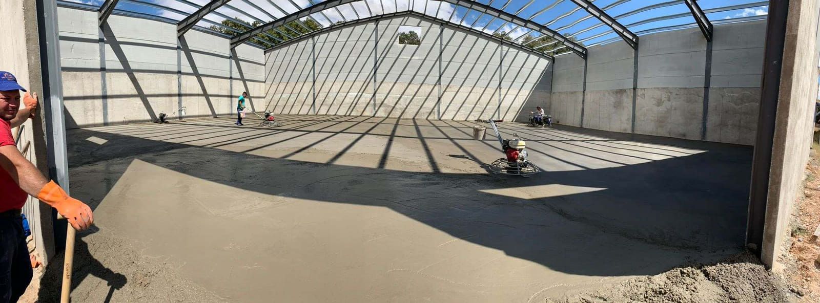 Obreros de la construcción vierten hormigón en un gran almacén. Un hombre usa una pala.